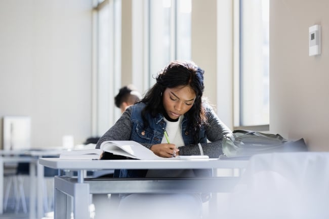 A young woman reads her textbook while taking notes
