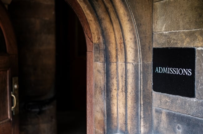 A sign reading "ADMISSIONS" hangs next to an archway on a stone building.