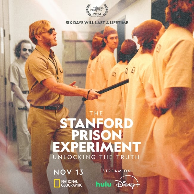 A poster for the 'Stanford Prison Experiment' limited series. A male student acting as a guard gestures with a baton toward a group of peers, dressed as prisoners, lined up and facing the other direction; text at the top states "Six days will last a lifetime." The poster also notes the series is streaming on Hulu and Disney+.