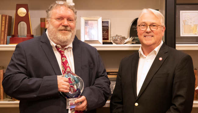 A photograph of Marshall Brain II, holding an award, standing next to North Carolina State University chancellor Randy Woodson.