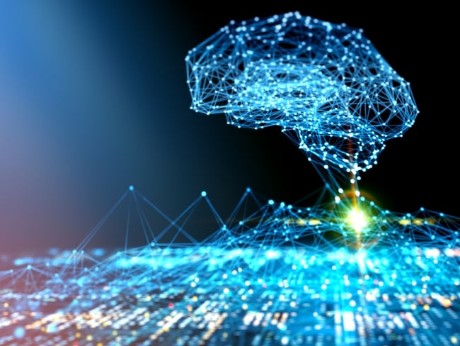 An illustration of artificial intelligence as a concept. An AI "brain" is brightly lit and hovers against a black background above a lit-up circuit board.