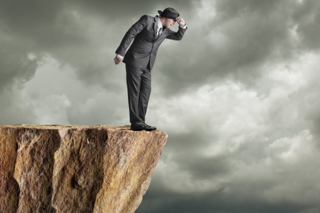 Man in blindfold and suit looks over cliff