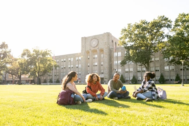 Four students sit on the lawn of a university quad. 