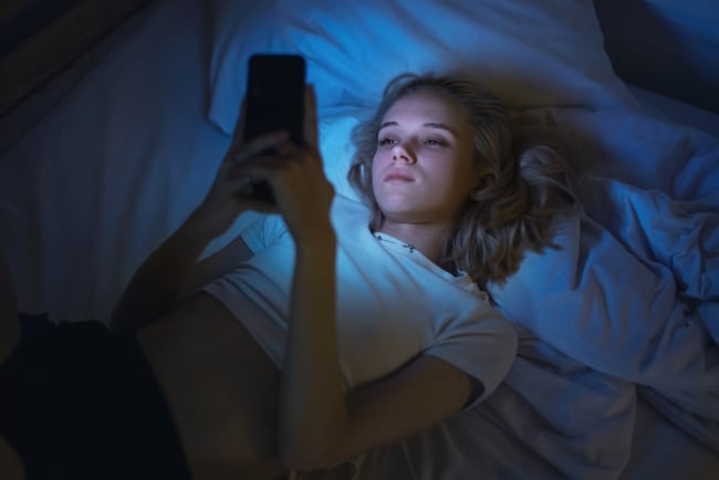 Young blonde woman in bed with mobile phone.