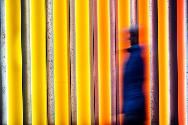 A blurred image of a person positioned toward the center-right of the frame, against a bright orange and yellow background.