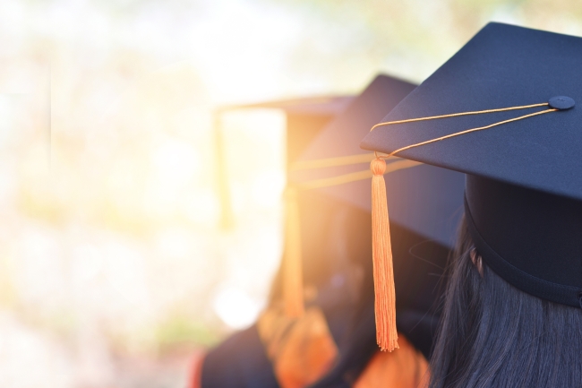 Three students in graduation caps stand in a row with their backs to the camera.