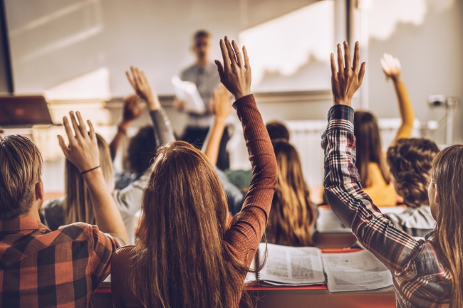 A rear view of a group of students in a lecture hall, raising their hands.