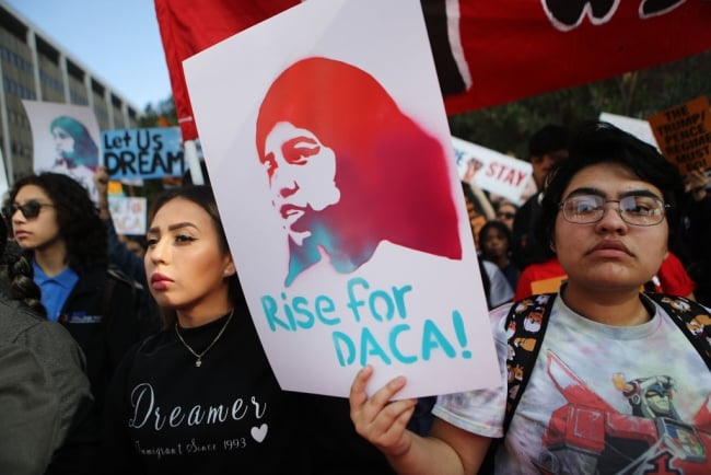 A student in a crowd holds up a sign that reads "Rise for DACA!"