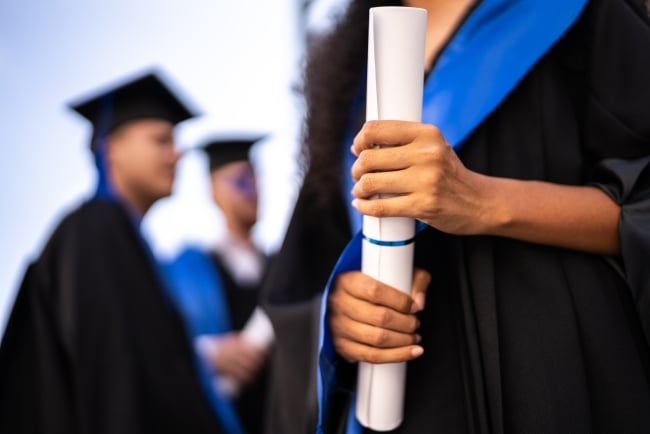 A close-up of a young woman in a graduation gown holding a diploma.