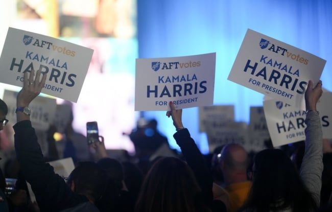 The picture depicts a group of attendees gathered to hear Kamala Harris speak to the American Federation of Teachers convention in Houston last year. Three attendees hold up signs that say "AFT Votes: Kamala Harris for President."
