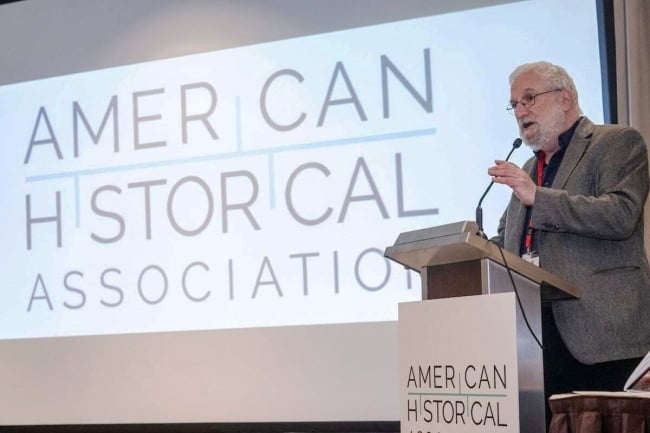 A photograph of Jim Grossman speaking into the mike at a lectern in front of a screen. Both the lectern and screen say "American Historical Association."