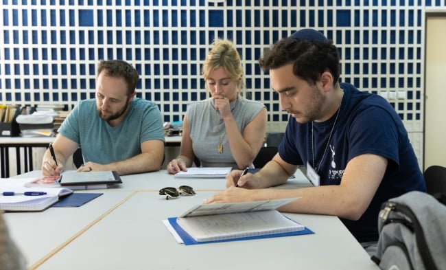 Three rabbinical students sit around a table looking at Jewish texts.
