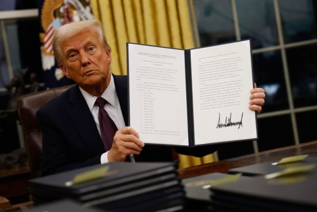 President Donald Trump, seated in the Oval Office, holds up an executive order signed on Jan. 20, 2025, the day of his inauguration.