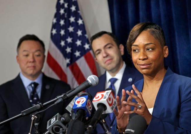Massachusetts attorney general Andrea Campbell, in a navy blue blazer, speaks a podium topped with several microphones