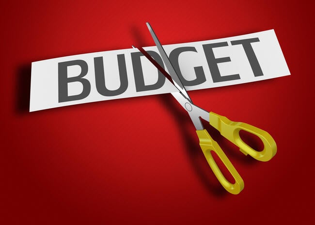 A pair of scissors cuts through a piece of paper with the word "BUDGET," against a red background.