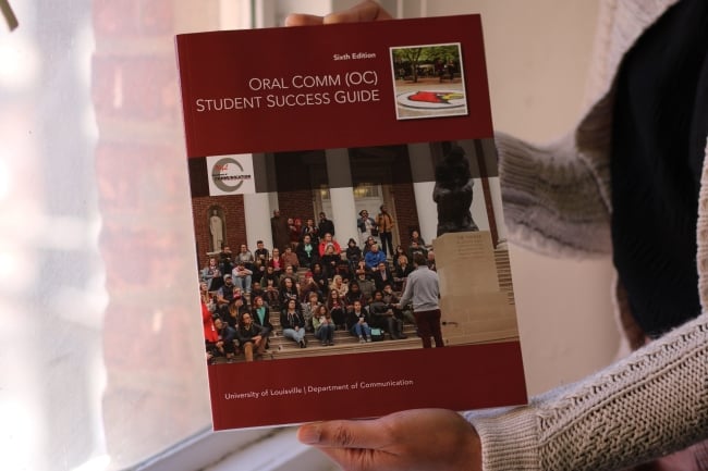 An unidentified person holds a printed version of the University of Louisville Oral Comm Success Guide