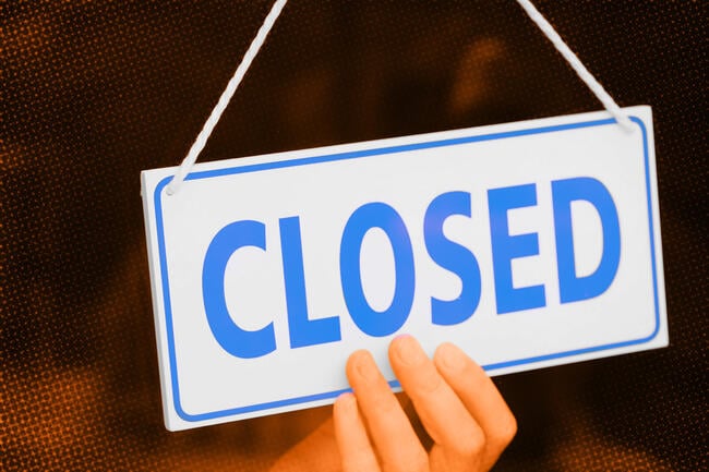 A hand holds up a hanging sign that says, in blue, "Closed."