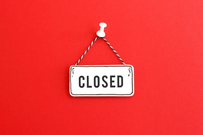 A photo of a handmade "closed" sign, on clapboard, tacked to a red background.
