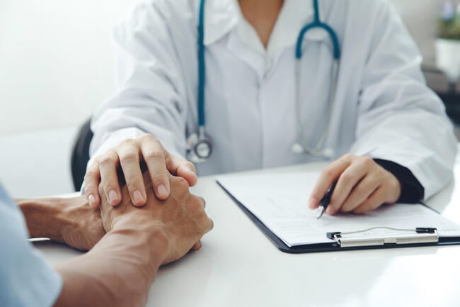 A close-up image of a doctor holding a patient's hand after a diagnosis.