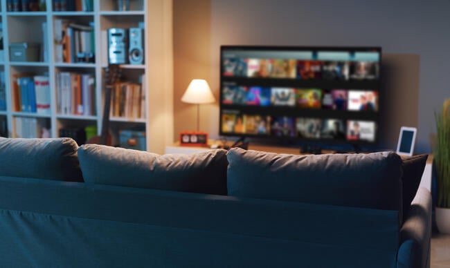 A photo of a relatively dark living room with the landing page for a streaming service visible on the TV, which sits next to a bookcase.