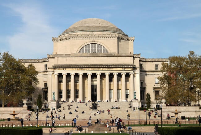 An image of the classical-style Low Memorial Library at Columbia University. Students can be seen sitting on its steps.