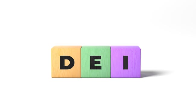 Three wooden alphabet blocks of different colors spell the acronym "DEI."