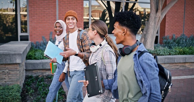 Four students walk to class on a college campus outside