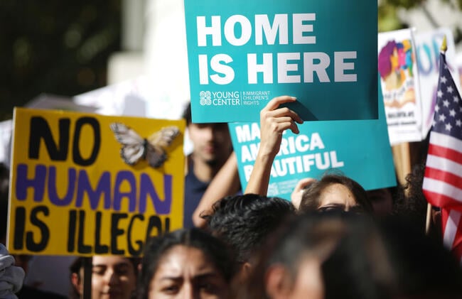 Students hold signs that read "no human is illegal" and "home is here."