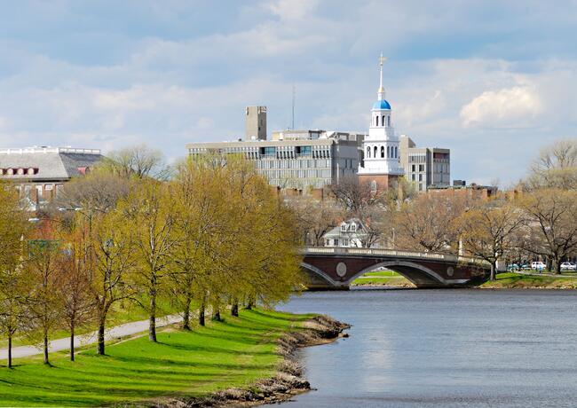 A photo of the Harvard University campus from across the Charles River in springtime, with leaves on trees just beginning to bud.