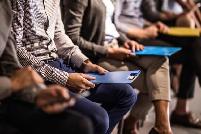 Large group of unrecognizable business people waiting for a job interview. Focus is on man a blue clipboard.