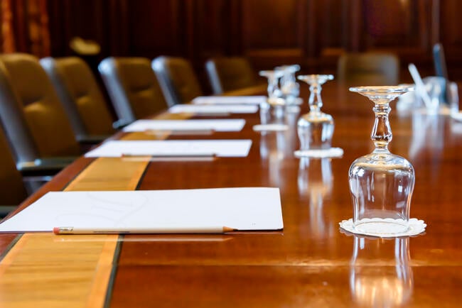 A photo of a wooden boardroom table, set up for a meeting, with pads of paper and water glasses.