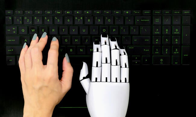 Human hand and a robot hand both hover over a computer keyboard.