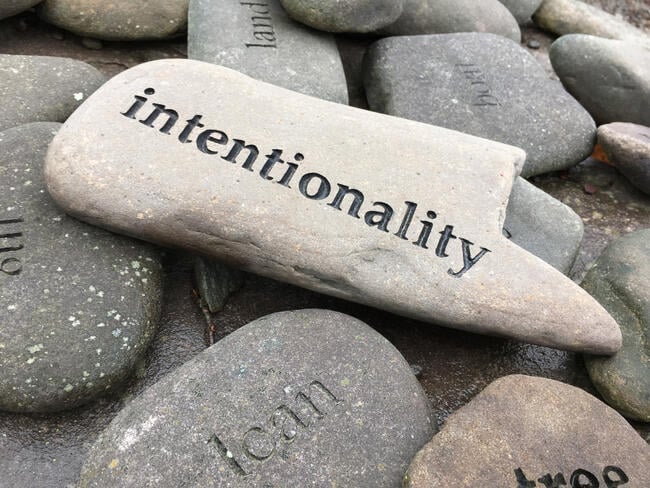 A photo of a pile of smooth stones, with the stone on top bearing the word “intentionality.”