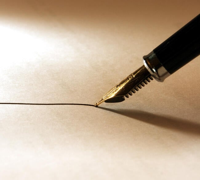 A close-up photo of a fountain pen with black ink being wielded to draw a thin line on paper.