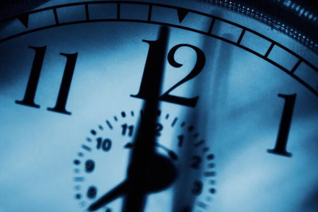 A close-up photo of a clock with a hand pointing to the 12.
