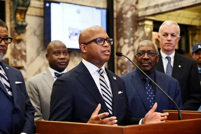 Former Jackson State University president Marcus Thompson speaks into a microphone at a podium with other JSU representatives behind him.