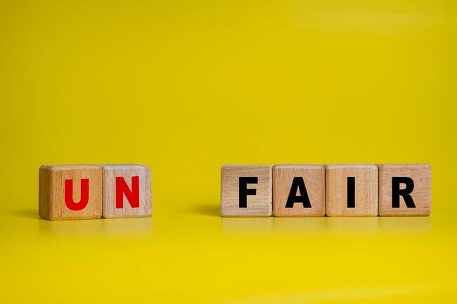 Six wooden alphabet blocks are juxtaposed against a bright yellow background in this illustration of the concept of fairness and unfairness. Two of the blocks read "UN" and are separated with a space from four more blocks that say "FAIR."