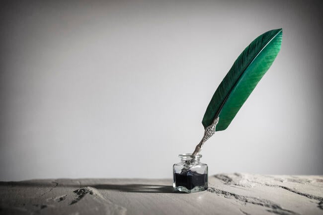 A quill pen in an ink pot against a gray background.