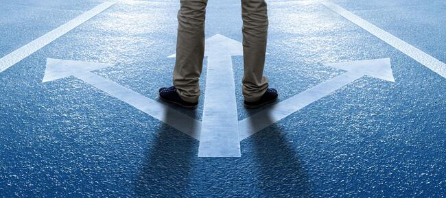 A photo of a man's legs standing on a set of painted arrows, pointing three different ways.