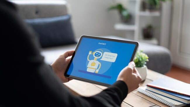 A close-up of a man holding a tablet with a chat bot open on the screen.