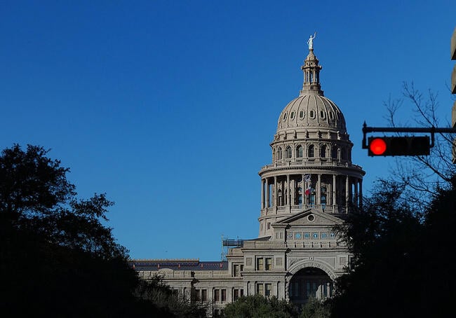 A photo of the Texas Capitol dome with a red stoplight in the foreground of the photo.