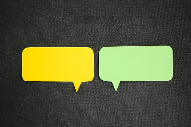A photo of two speech bubbles, one yellow and one green, against a dark background.
