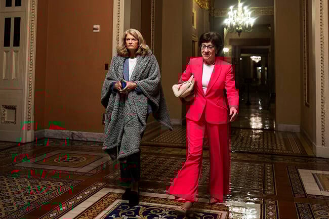 U.S. Sen. Lisa Murkowski (R-AK) and U.S. Sen. Susan Collins (R-ME) walk to the Senate floor during overnight votes at the U.S. Capitol. Murkowski has a blanket wrapped around her shoulders and Collins is wearing a red suit.