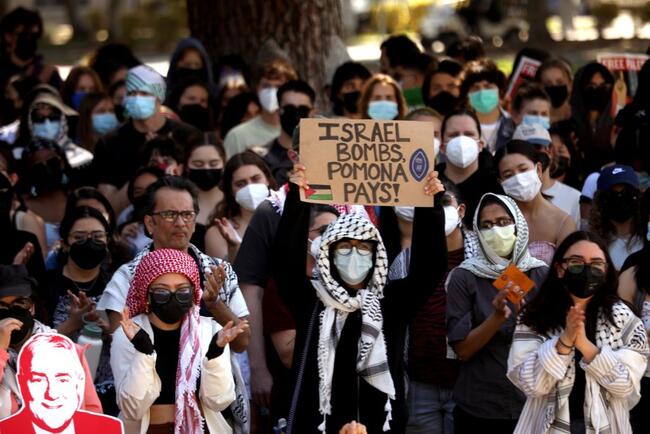 Masked protesters stand or march, with one wearing a keffiyeh and holding a sign saying “Israel bombs, Pomona pays!”