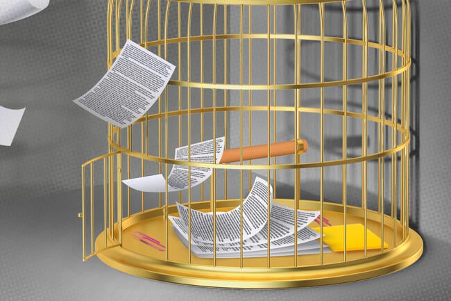 An open bird cage with papers fluttering through the door with other desk supplies on the cage floor. 
