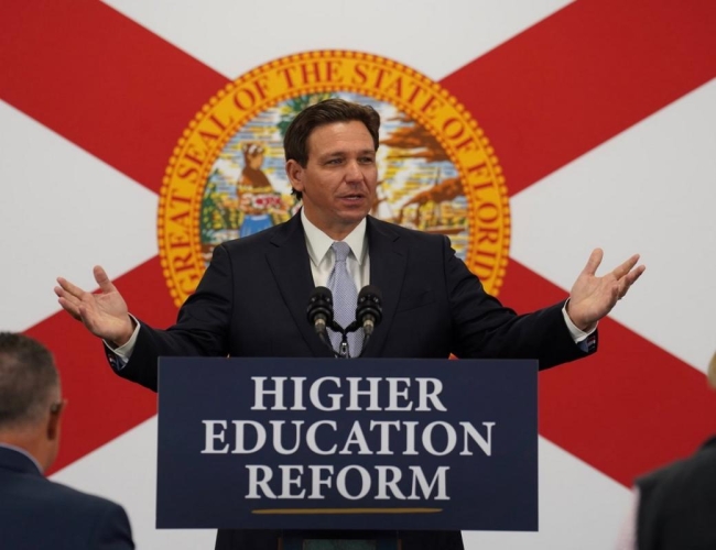 Florida governor Ron DeSantis standing in front of a Florida flag and behind a podium with a sign that says "Higher education reform"