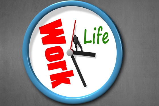Clock with "Work" written in red taking up more than half of the face of the clock and "life" in green taking up about a fourth, while a man stands on the hands at 3:30 trying to push back the work section