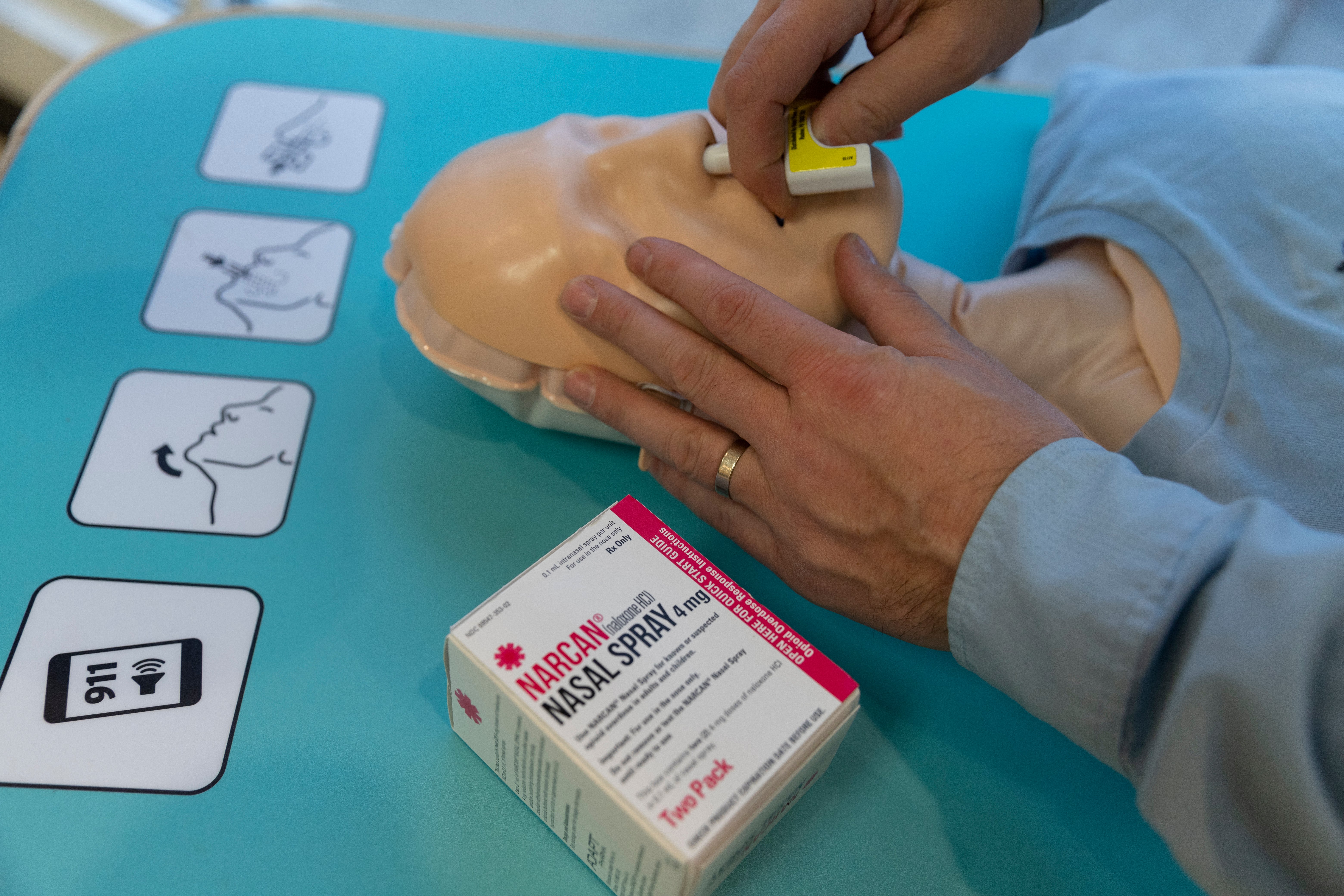 Close-up of the head of a training dummy, with a person demonstrating how to administer the NARCAN nasal spray.