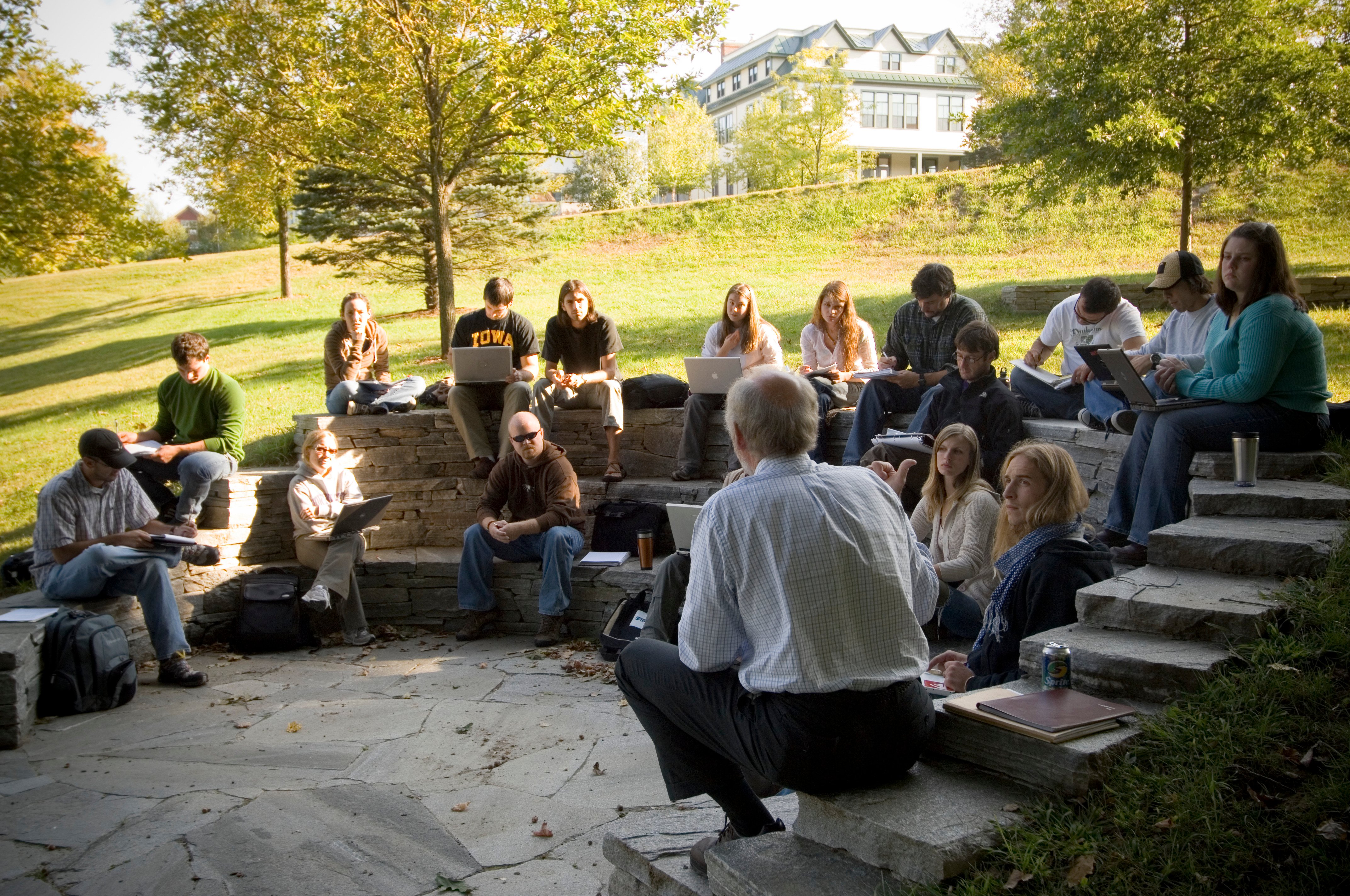 A professor and students hold a class outside on a green Vermont hillside.