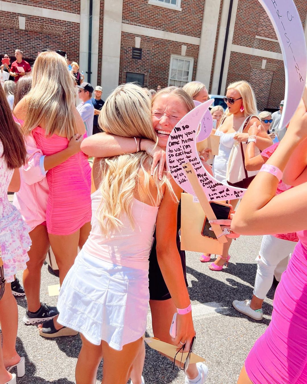 A blonde woman hugs another blonde woman in a crowd of women, many of whom are wearing pink.